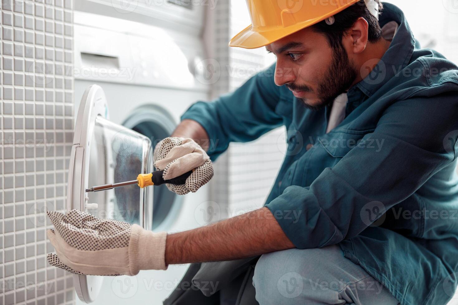 Focused repairman in worker suit is fixing washing machine in bathroom photo