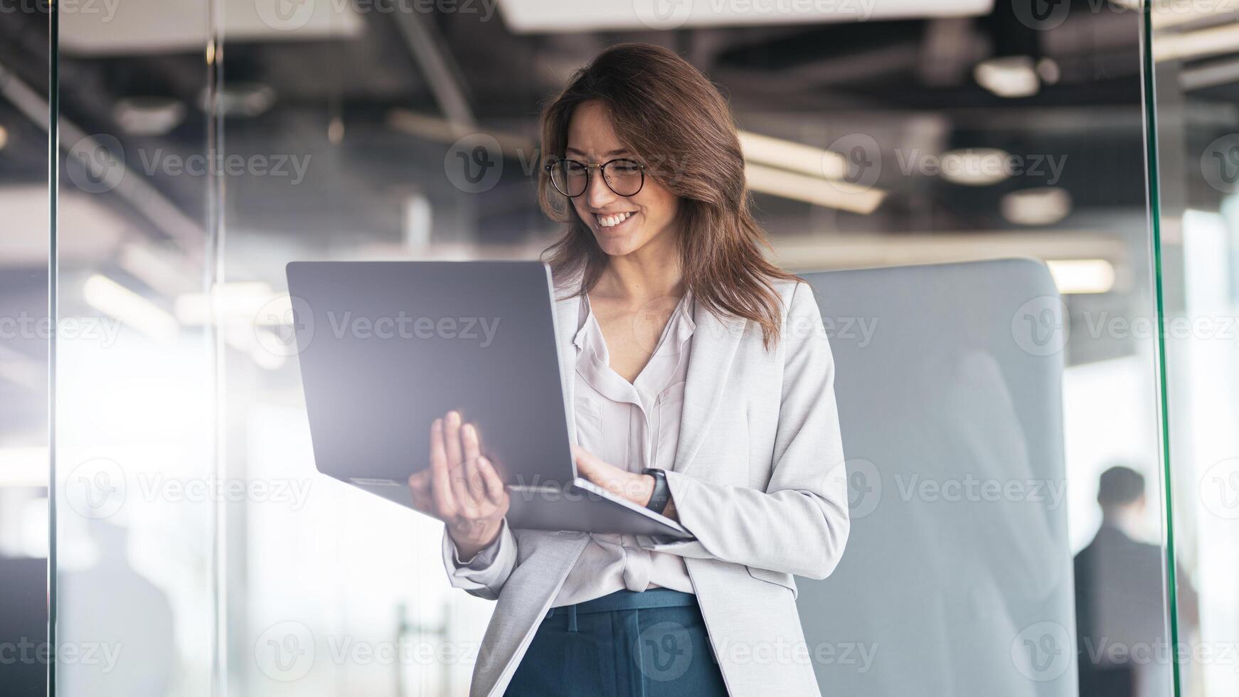 Smiling businesswoman at office with group of colleagues on background, working on laptop photo