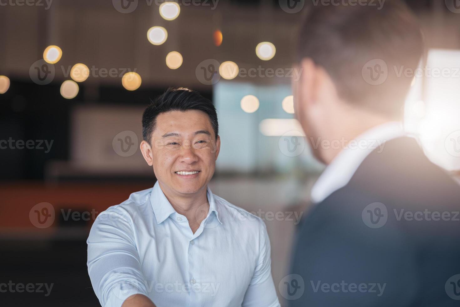 Close up of two smiling businessmen are handshaking after a successful deal in modern office photo