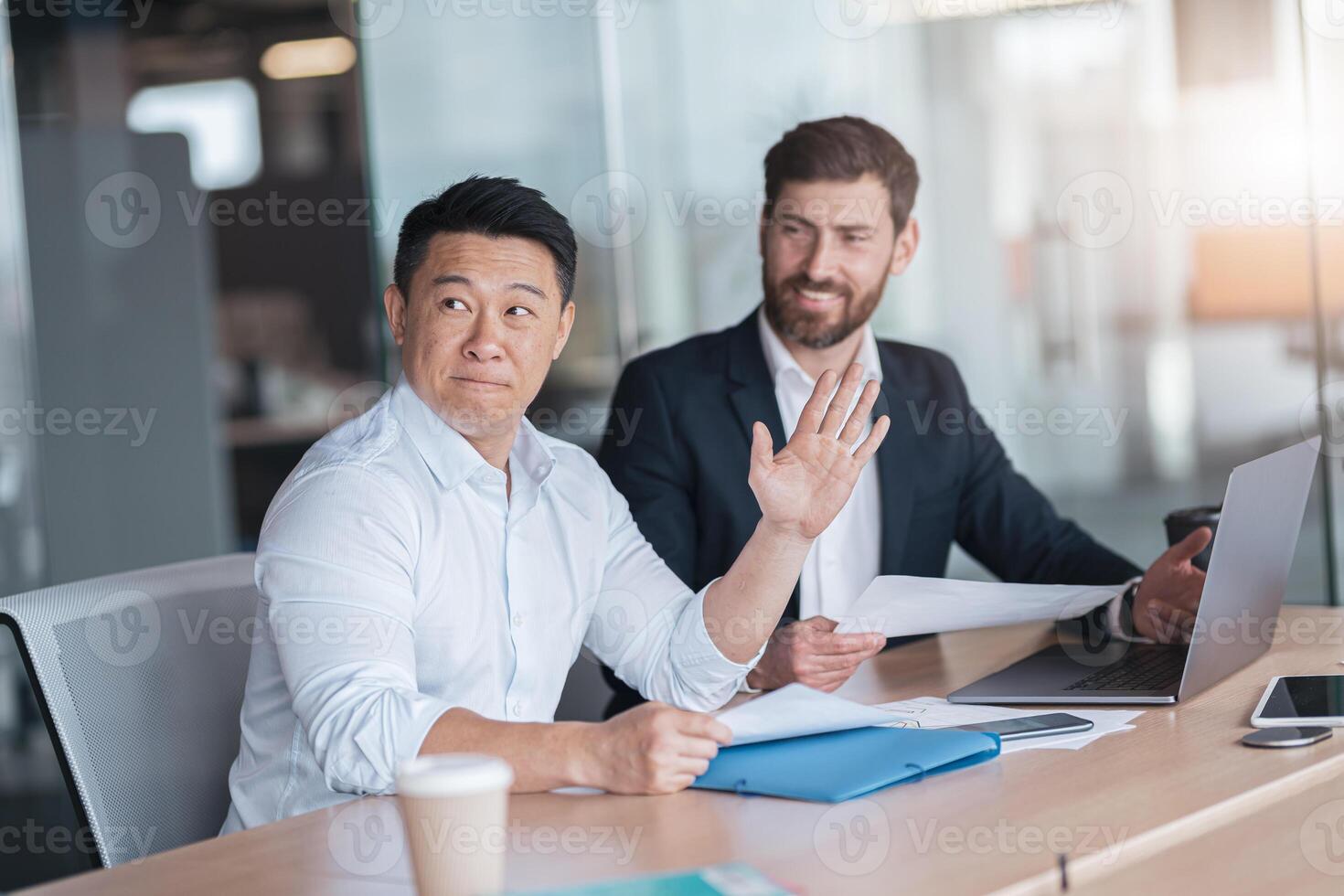 Focused Asian businessman in a meeting raises his hand to participate in a discussion photo