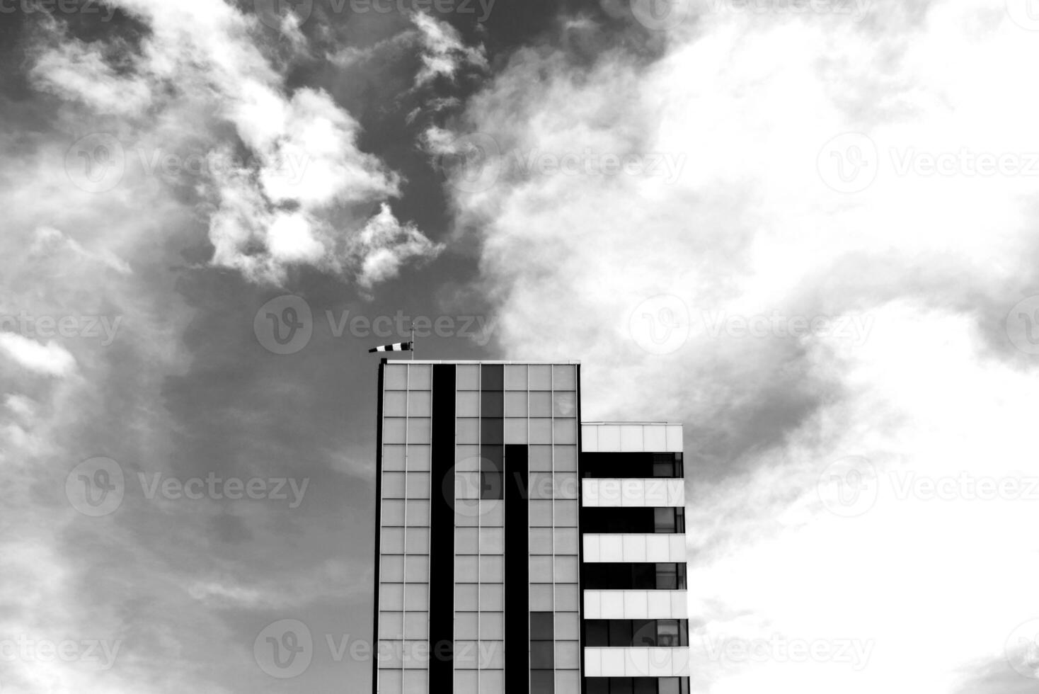 Black and white modern glass building with a wind sock on the roof against a dramatic cloudy sky. photo