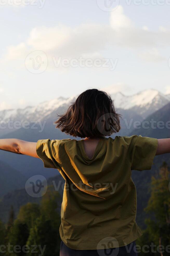 Back view of a young woman standing with open arms, enjoying the breathtaking mountain landscape. symbolizing freedom, adventure, and connection with nature photo