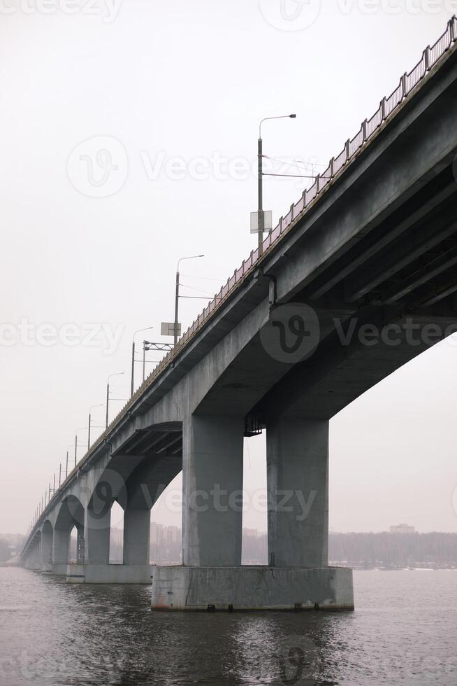 Large concrete bridge spanning a wide river on an overcast day. The perspective emphasizes the structure's scale and architectural details. photo