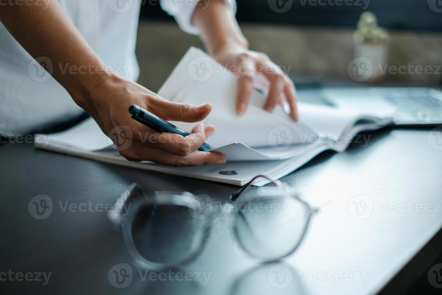 Close-up of hands writing on documents at a desk with glasses, showcasing a professional office environment. photo
