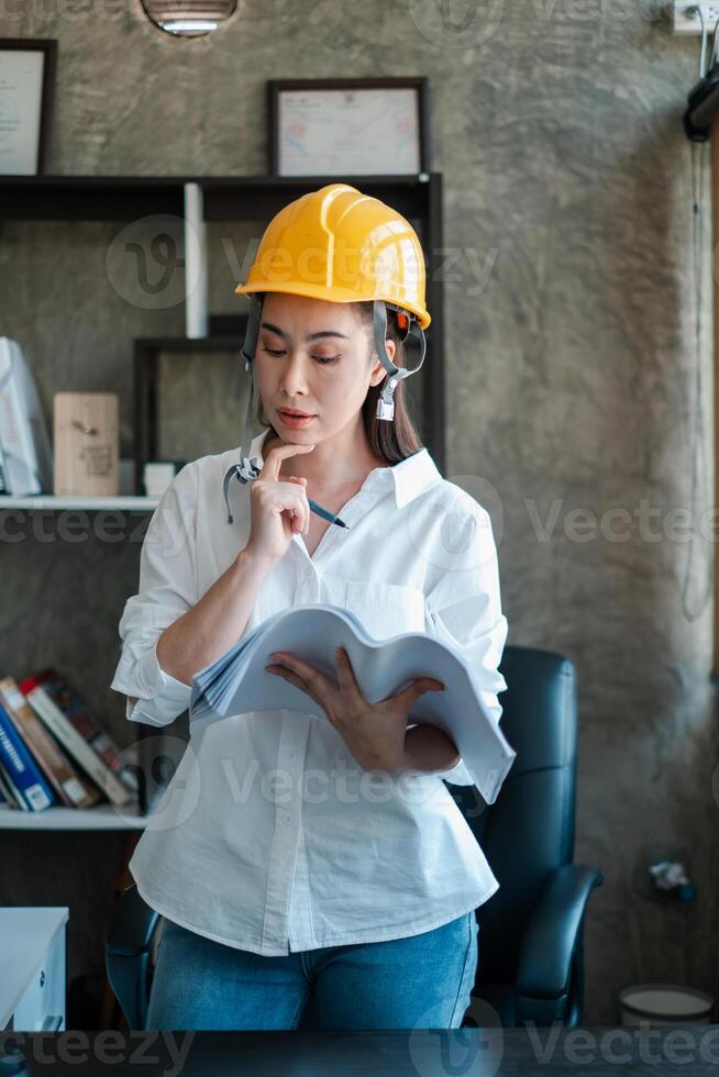 Female engineer wearing a hard hat examines blueprints in a contemporary office, highlighting construction and planning. photo