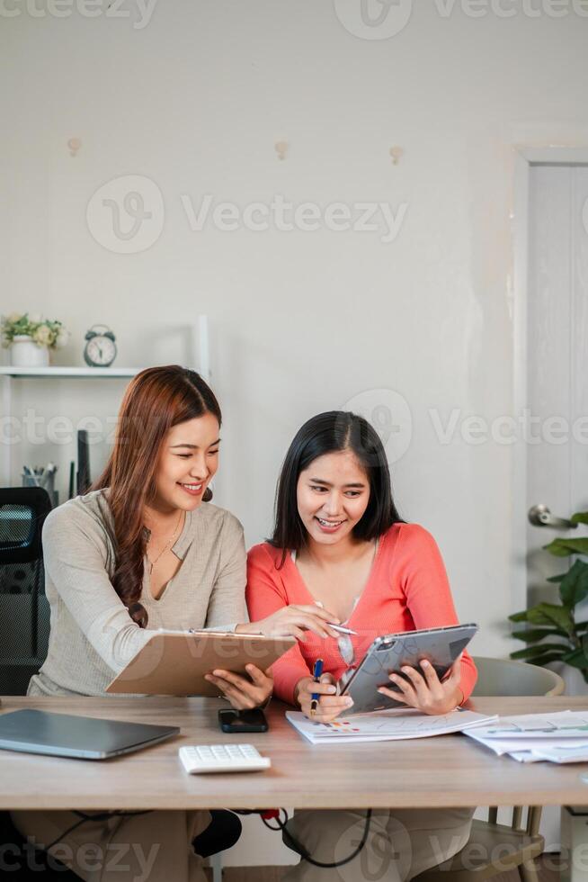 Two women working together in a modern office, using a tablet and documents for business planning and collaboration. photo