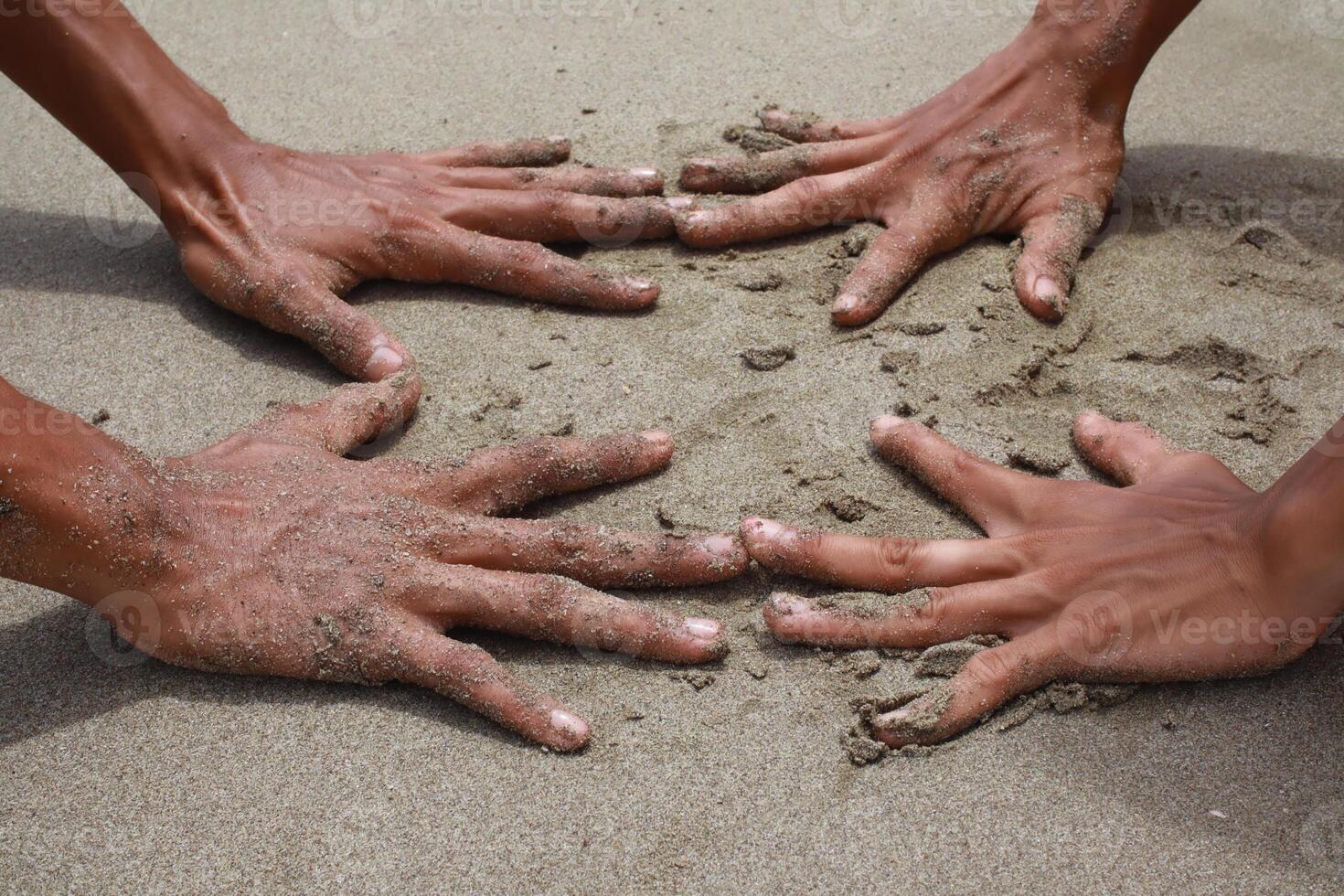 Four sandy hands uniting on the sand, illustrating beach togetherness, unity, or teamwork photo