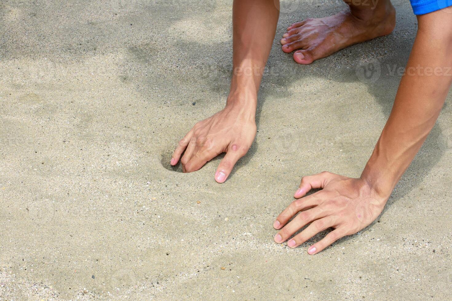 The Man's Hands Are Digging A Hole In The Sandy Beach On A Sunny Day photo