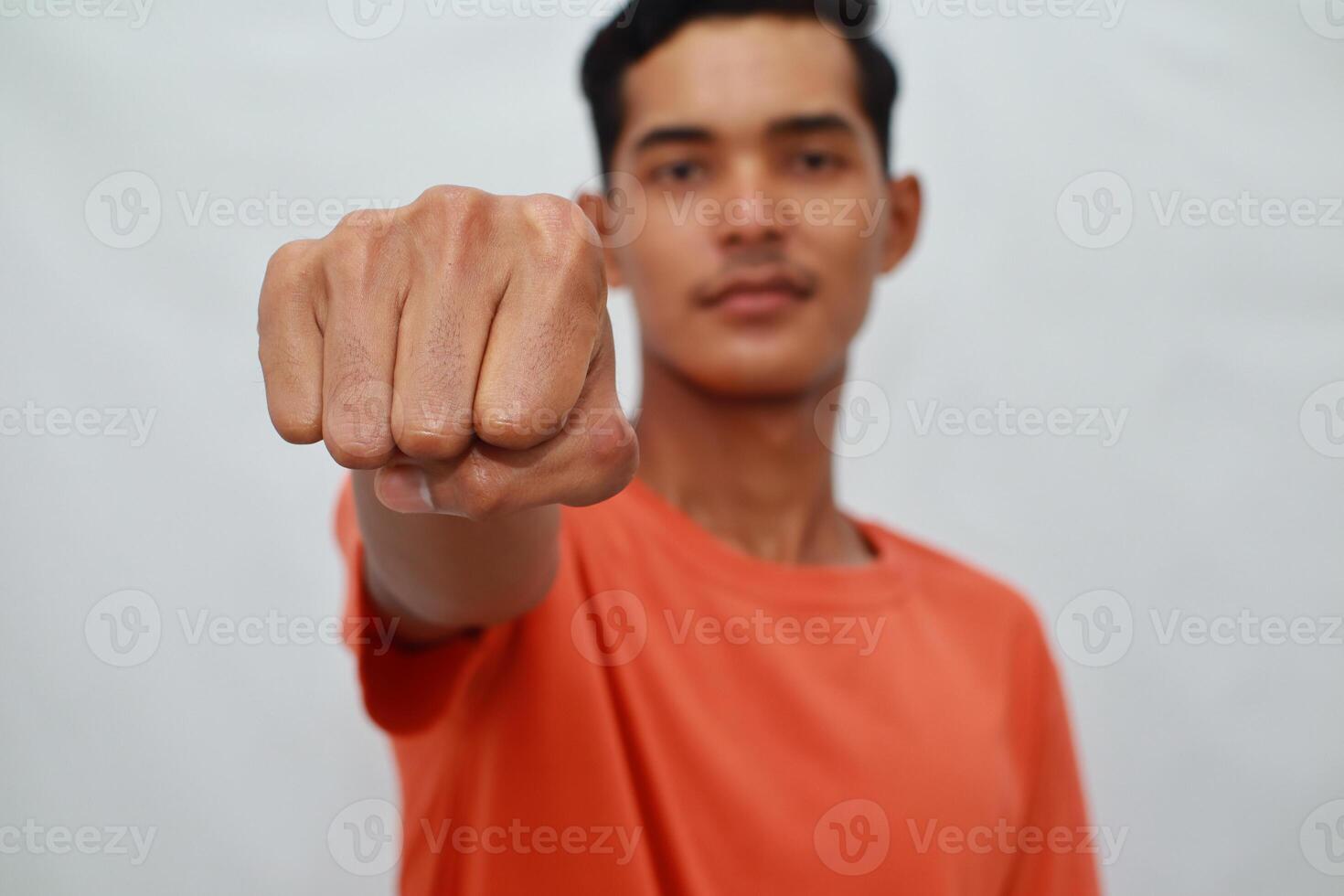 Close Up Portrait Of A Young Man With Clenched Fist, Wearing An Orange T Shirt Against A White photo