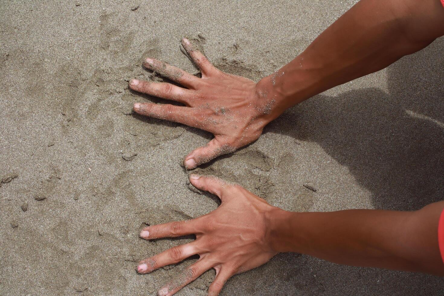A man's palms press into the texture of the beach sand, making temporary marks photo