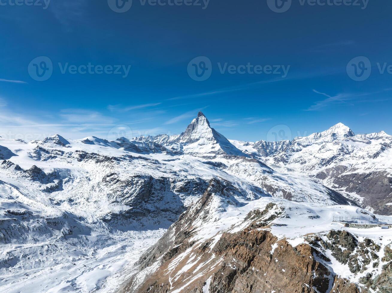 Snow covered Matterhorn mountain near Zermatt, Switzerland, with a rocky ridge and observatory under a clear blue sky in an alpine setting. photo