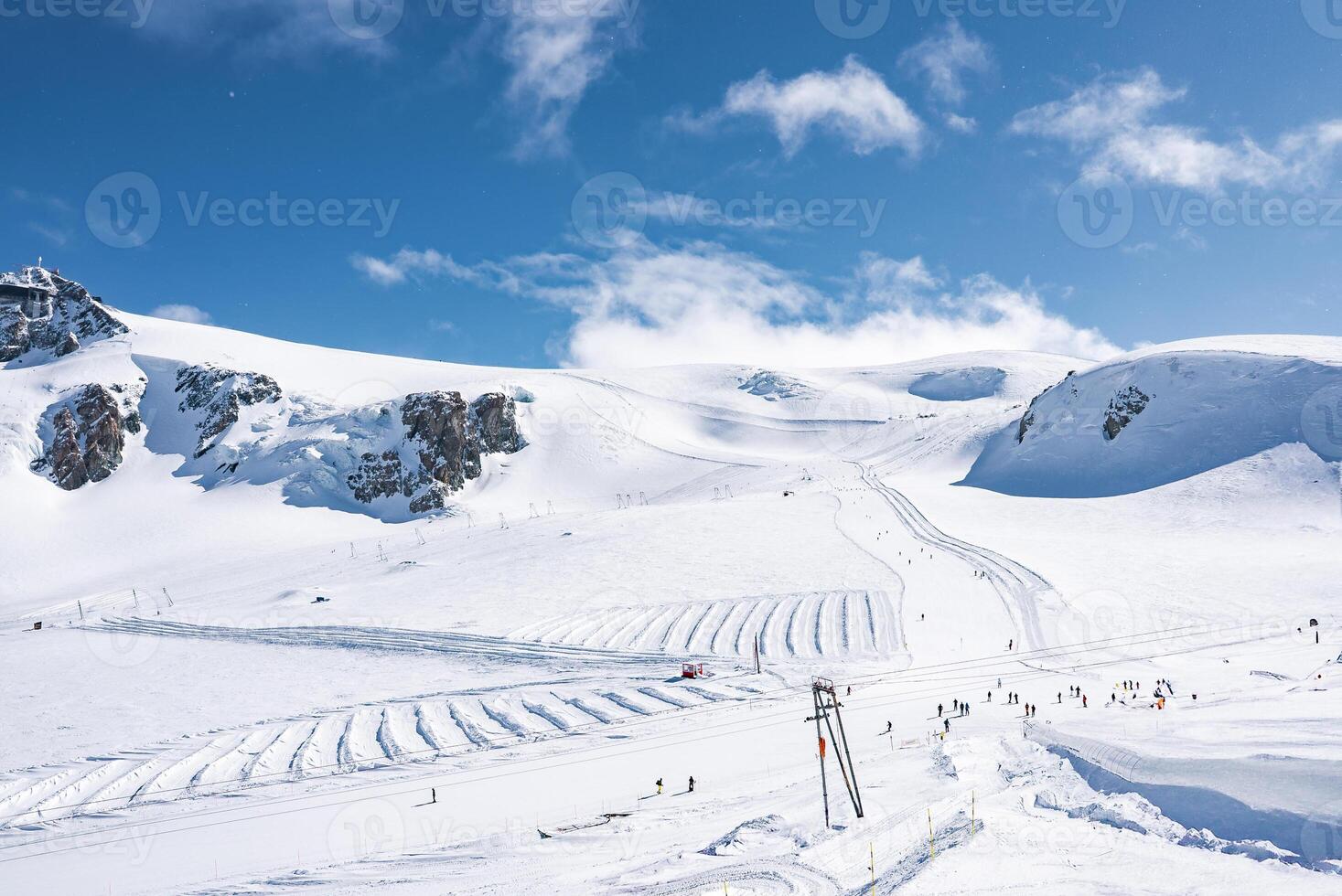 Snow covered peaks and ski slopes at Zermatt ski resort, Switzerland, with a ski lift in the foreground and skiers enjoying the winter terrain. photo