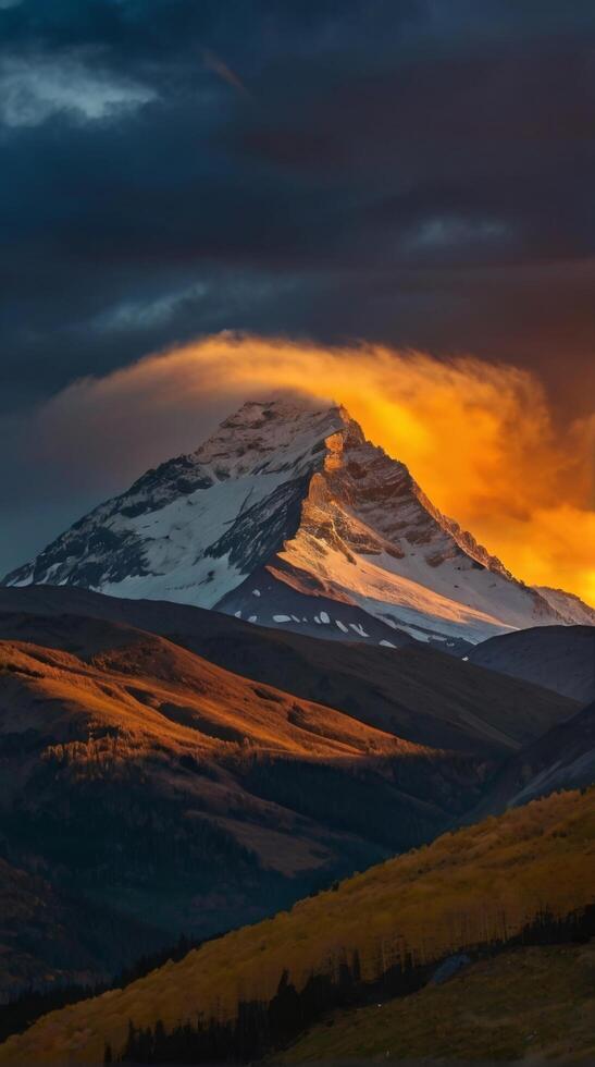 The sun sets over a mountain with snow capped peaks photo