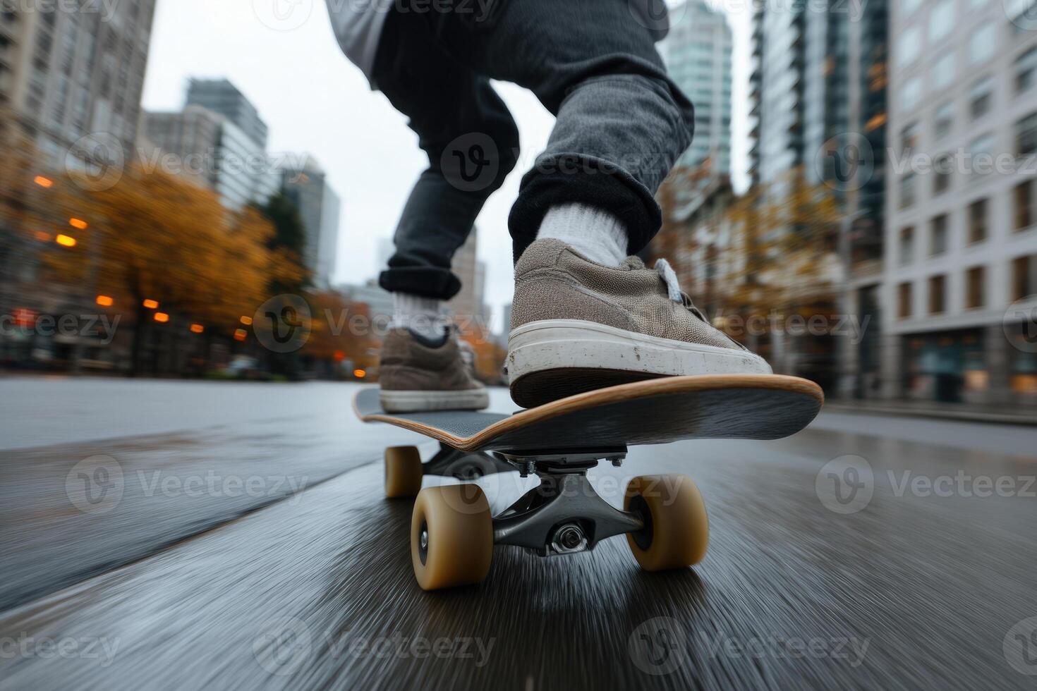 A person skillfully rides a skateboard along a wet urban road amid tall skyscrapers. The ground glistens with rain, showcasing the cloudy atmosphere of the city photo