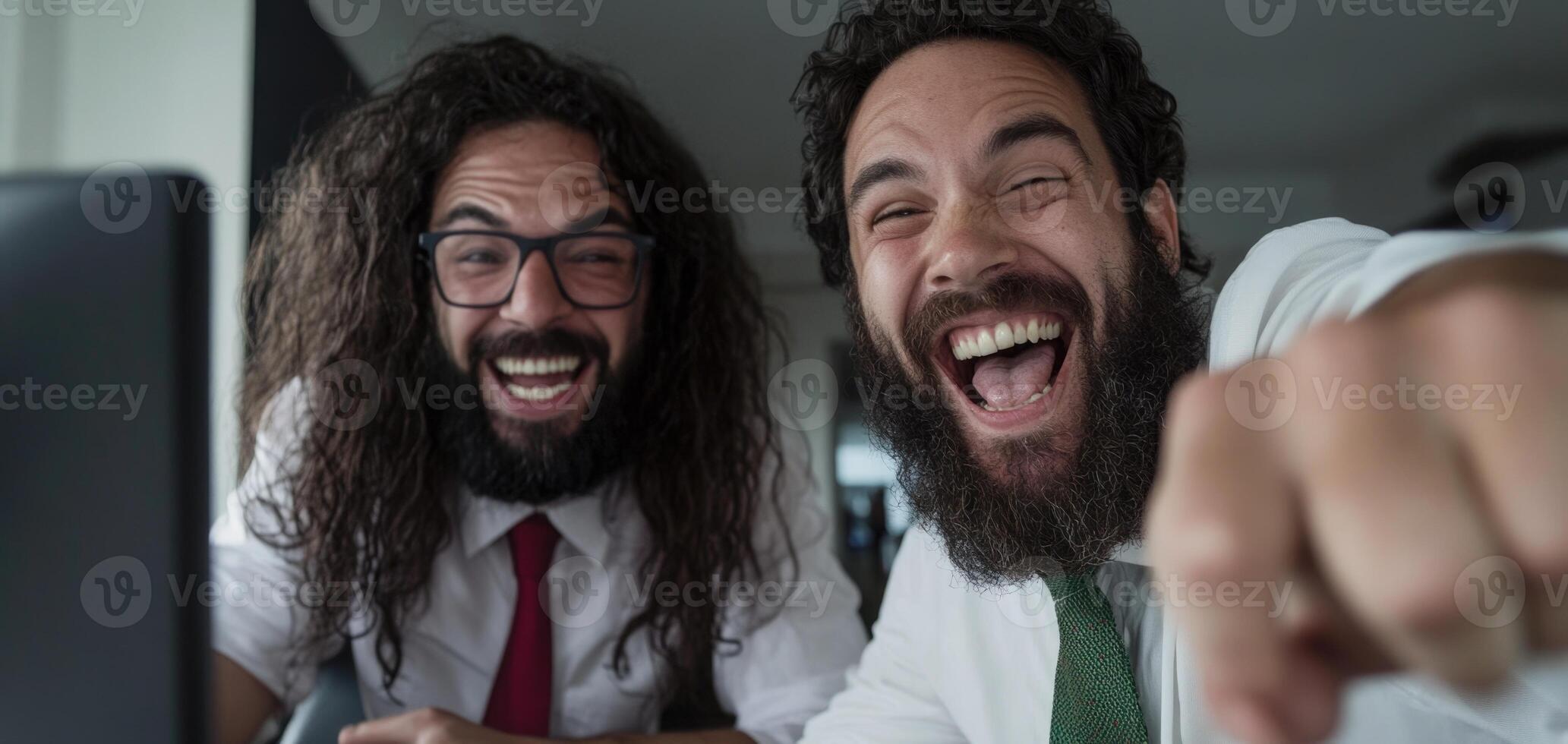 Two bearded men laughing while using a computer photo