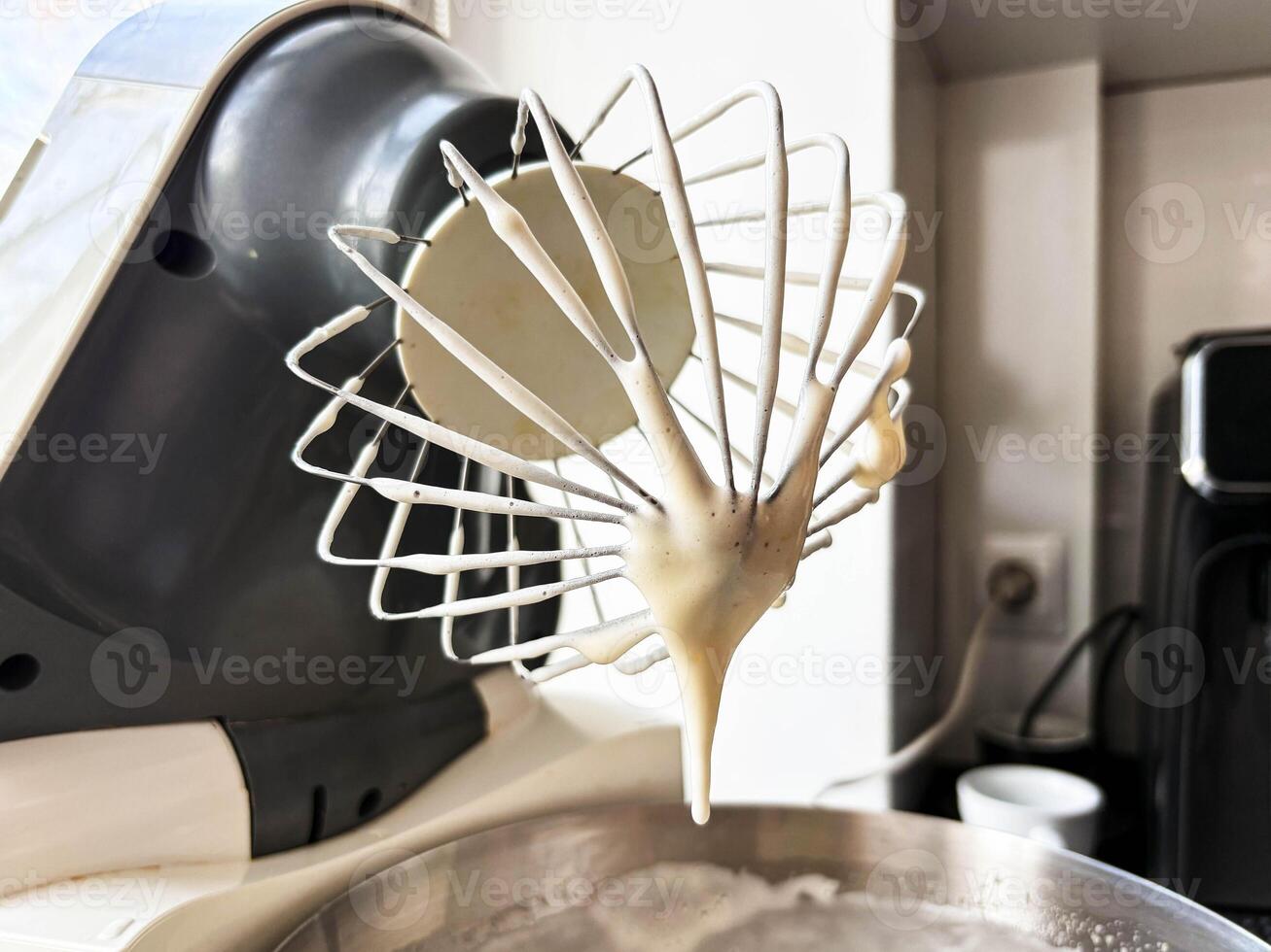 Close-up of dough dripping from a metal whisk. Making dough in a stand mixer at home. photo