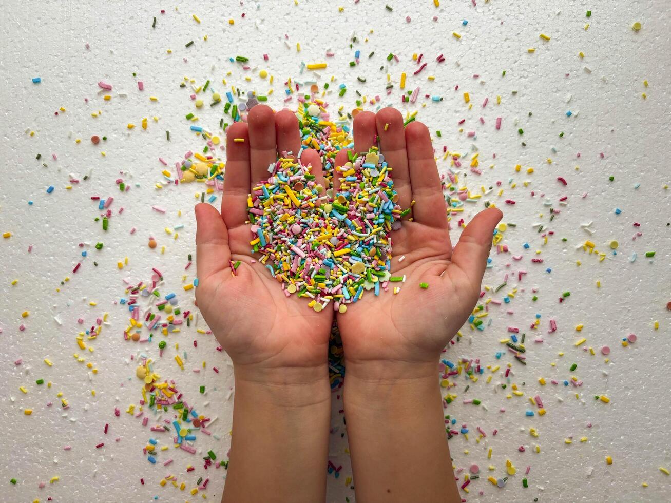 Child's hands are covered with multi-colored sugar sprinkles and form a heart shape. Child plays photo
