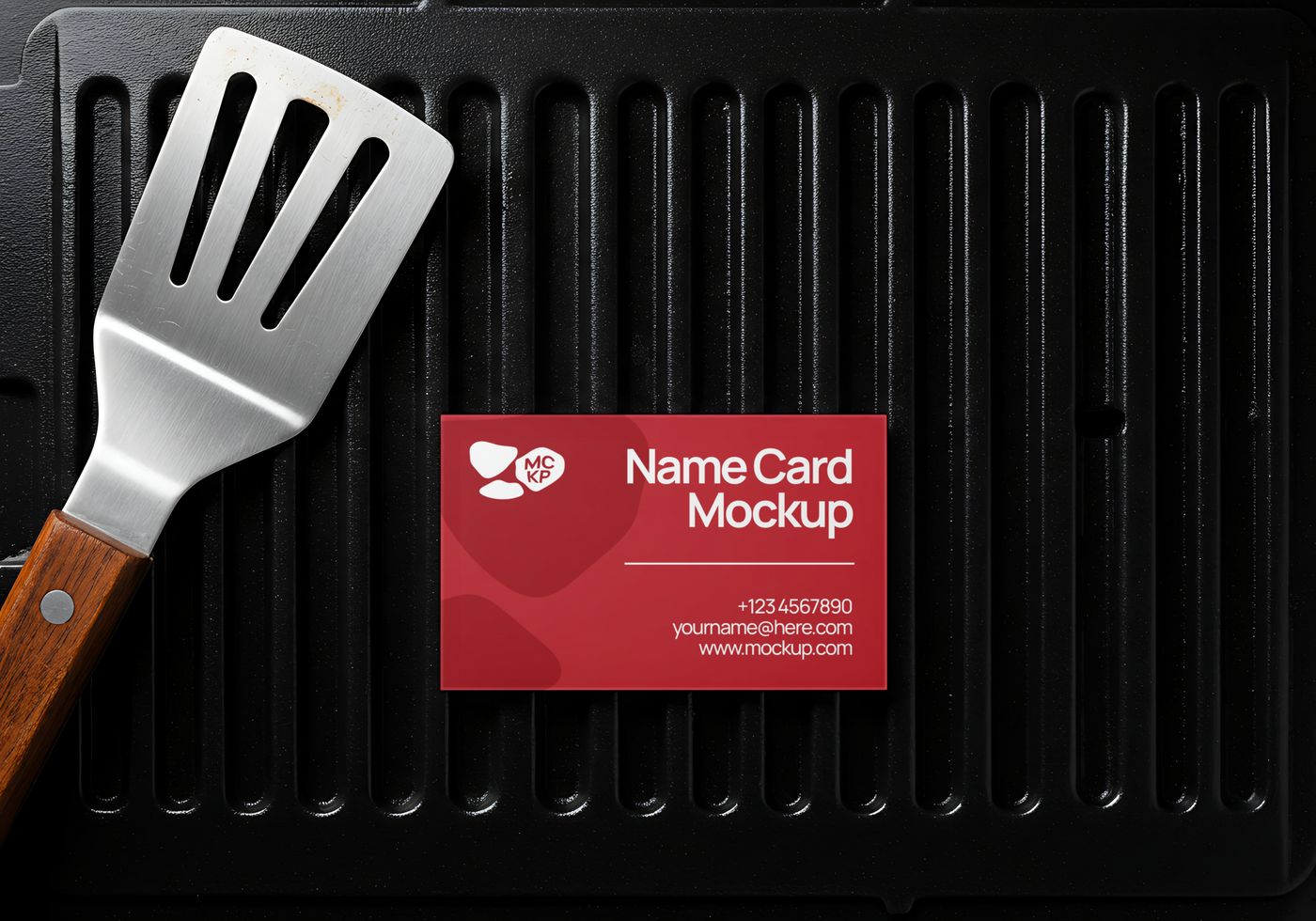 A grilling spatula and a name card mockup rest on a black grill psd