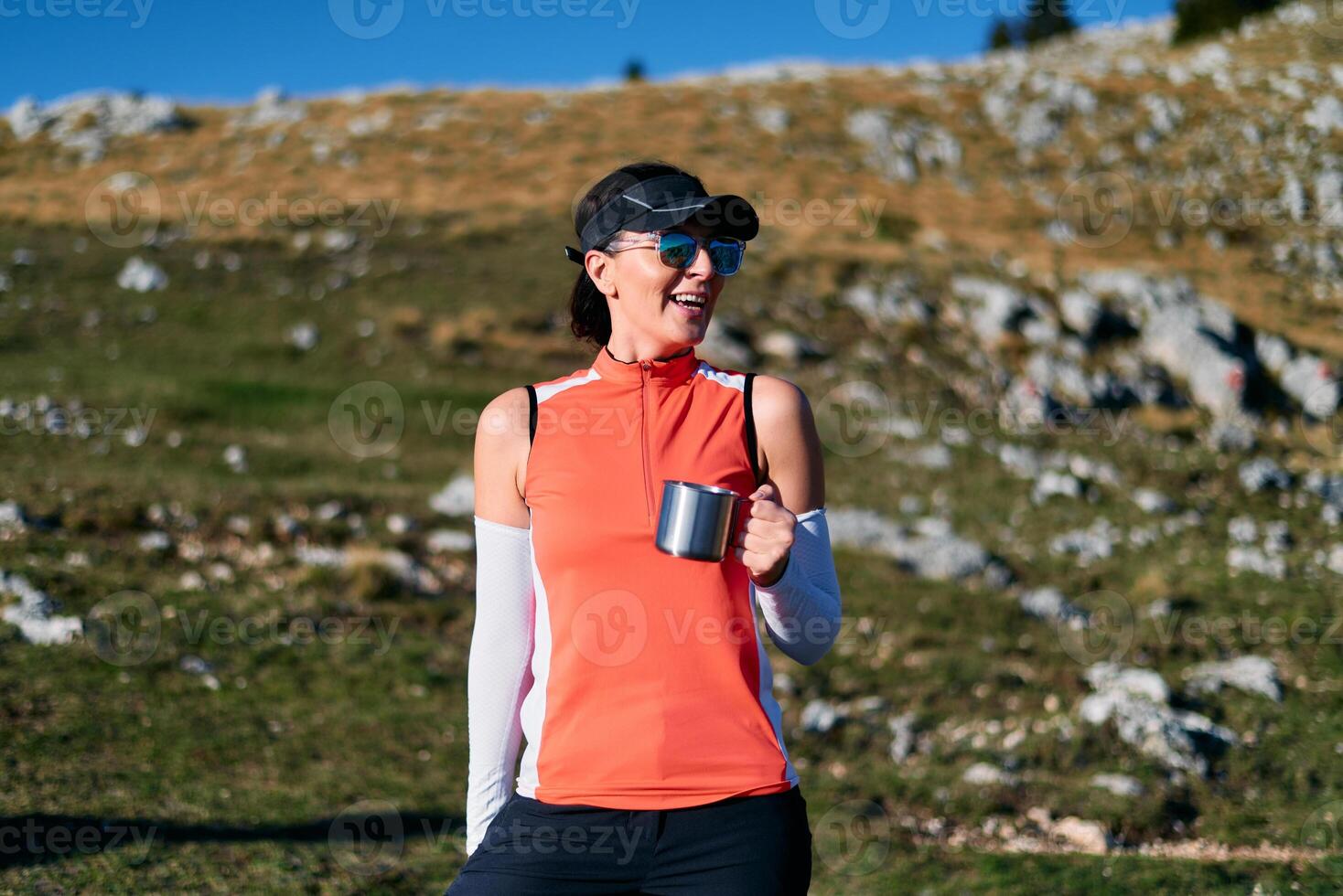 A female hiker enjoys a warm cup of tea while resting after a challenging mountain climb.A woman hiker takes a peaceful break, sipping tea and enjoying the view after a strenuous mountain climb photo