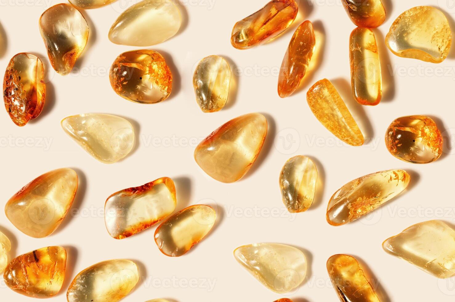 Amber stones on light beige background, minimal monochrome seamless pattern, transparent stone yellow beige color. Natural gemstone mineral. Top view Amber texture. Nature gems at sunlight photo