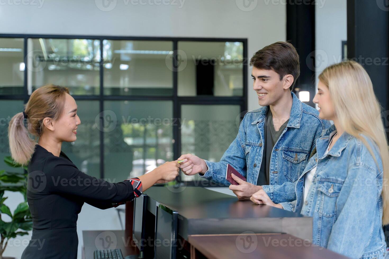 Smiling hotel receptionist handing keycard to guests at check-in counter, showing friendly customer service and hospitality in modern travel setting photo