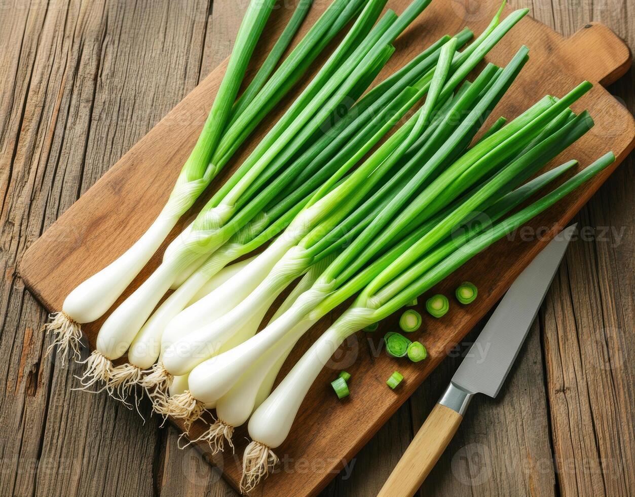 Fresh green onions on wooden cutting board with knife nearby photo