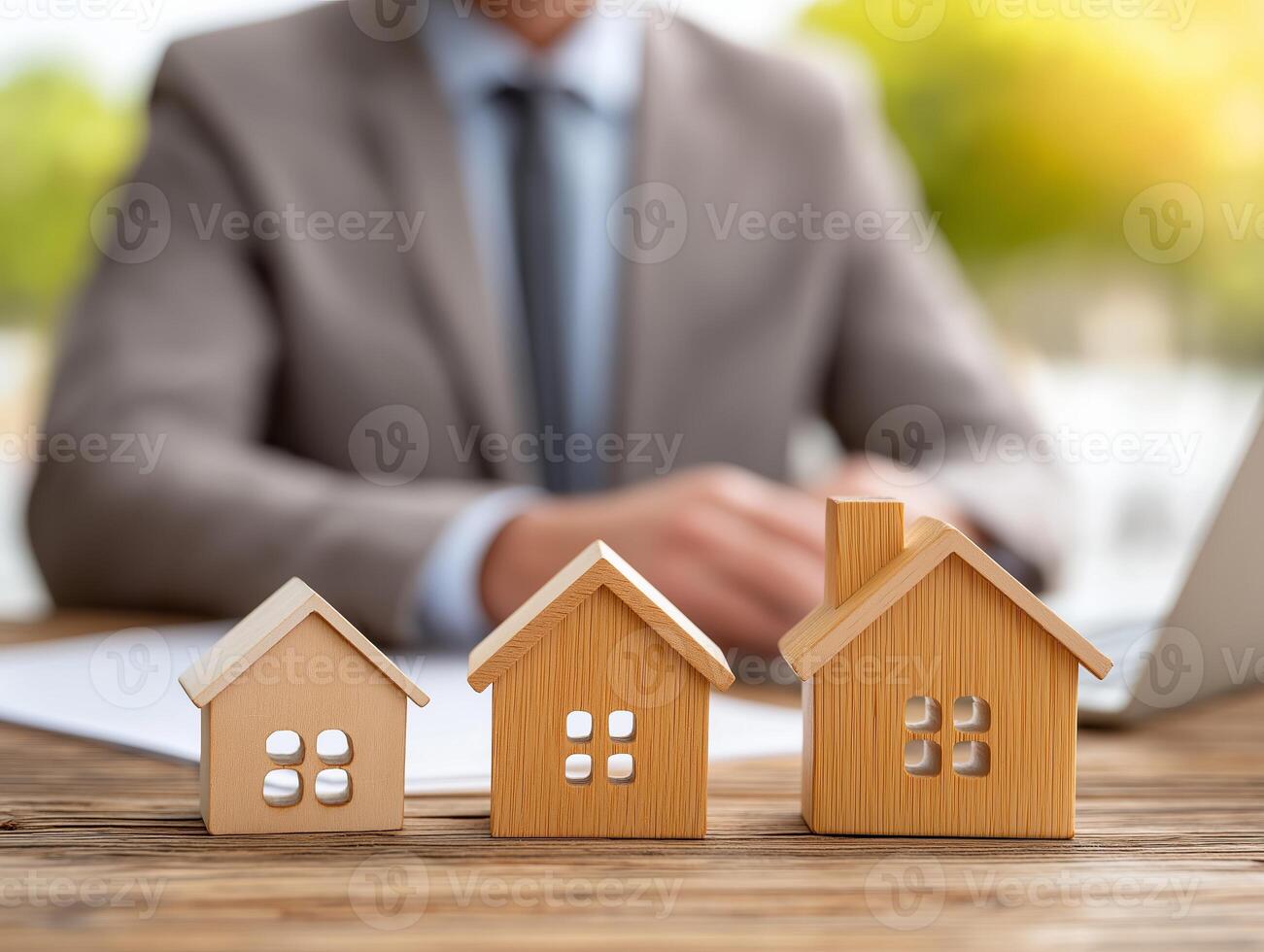 Real estate agent focused on laptop at modern workspace with wooden home models and contract documents. Real estate agent is diligently working on a laptop at a pro desk filled with wooden home models photo