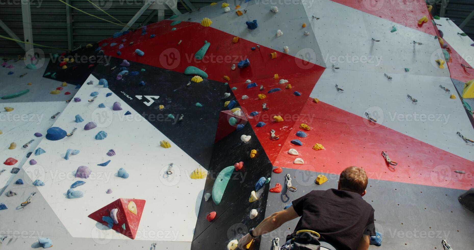 A young man equipped with climbing harnesses climbs up a climbing wall photo