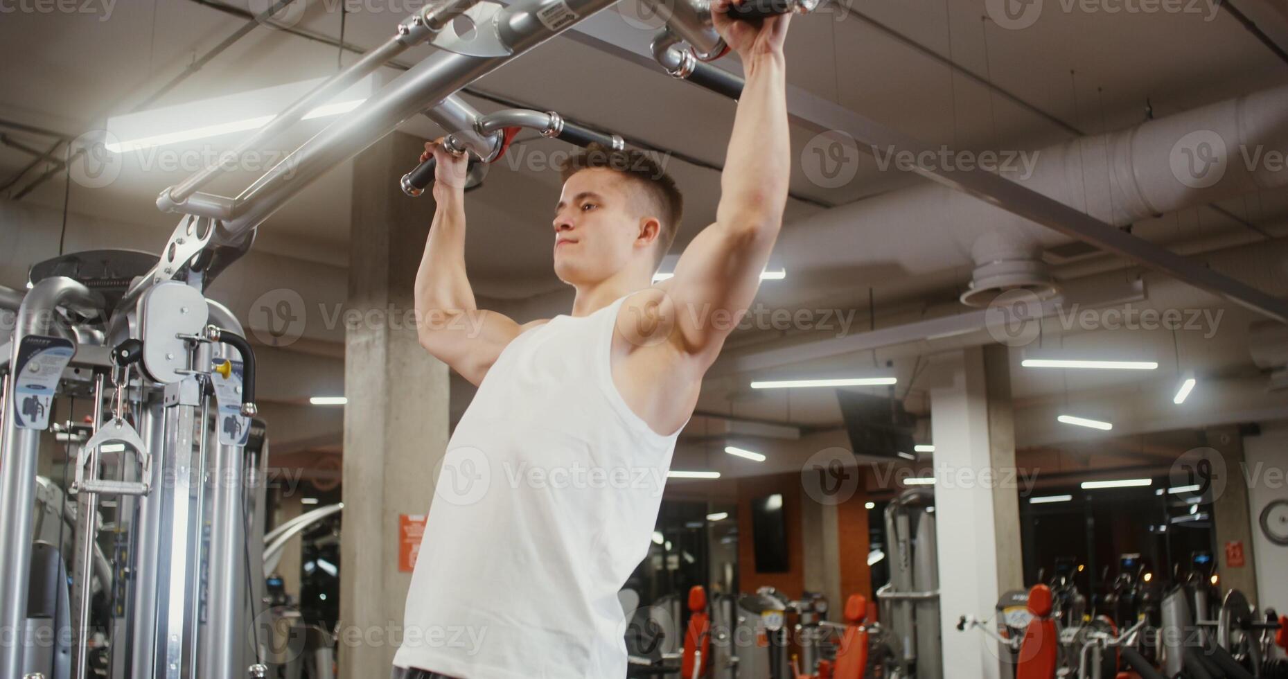 A young man is doing pull-ups on the simulator, doing in a modern gym photo