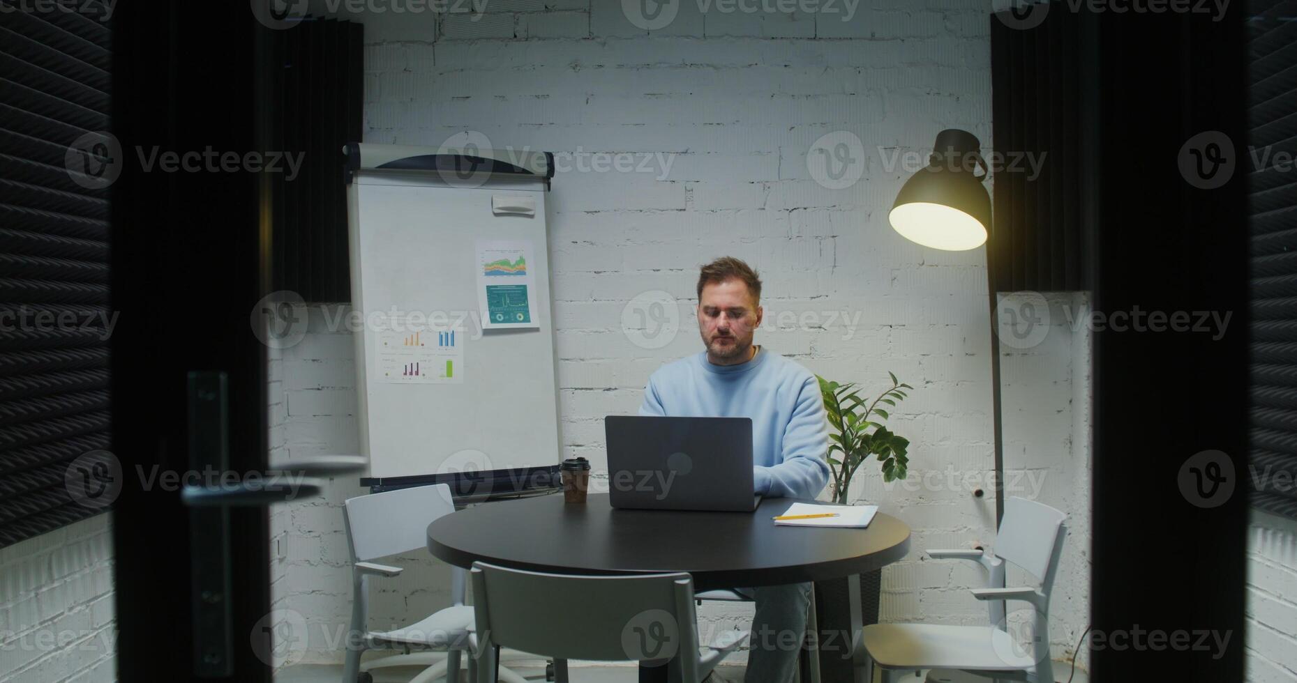 A young man works at a laptop, sitting alone in a meeting room photo
