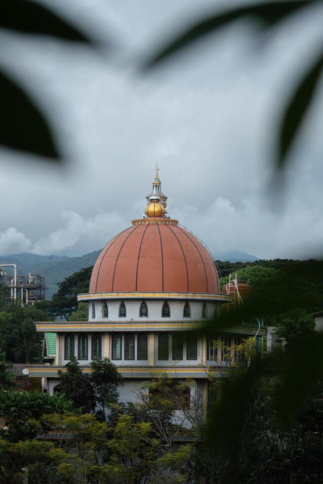 The mosque's stunning gold and white dome, adorned with the word Allah, stands gracefully against a bright blue sky with fluffy clouds. As a sacred place of worship for Muslims, it exudes beauty photo