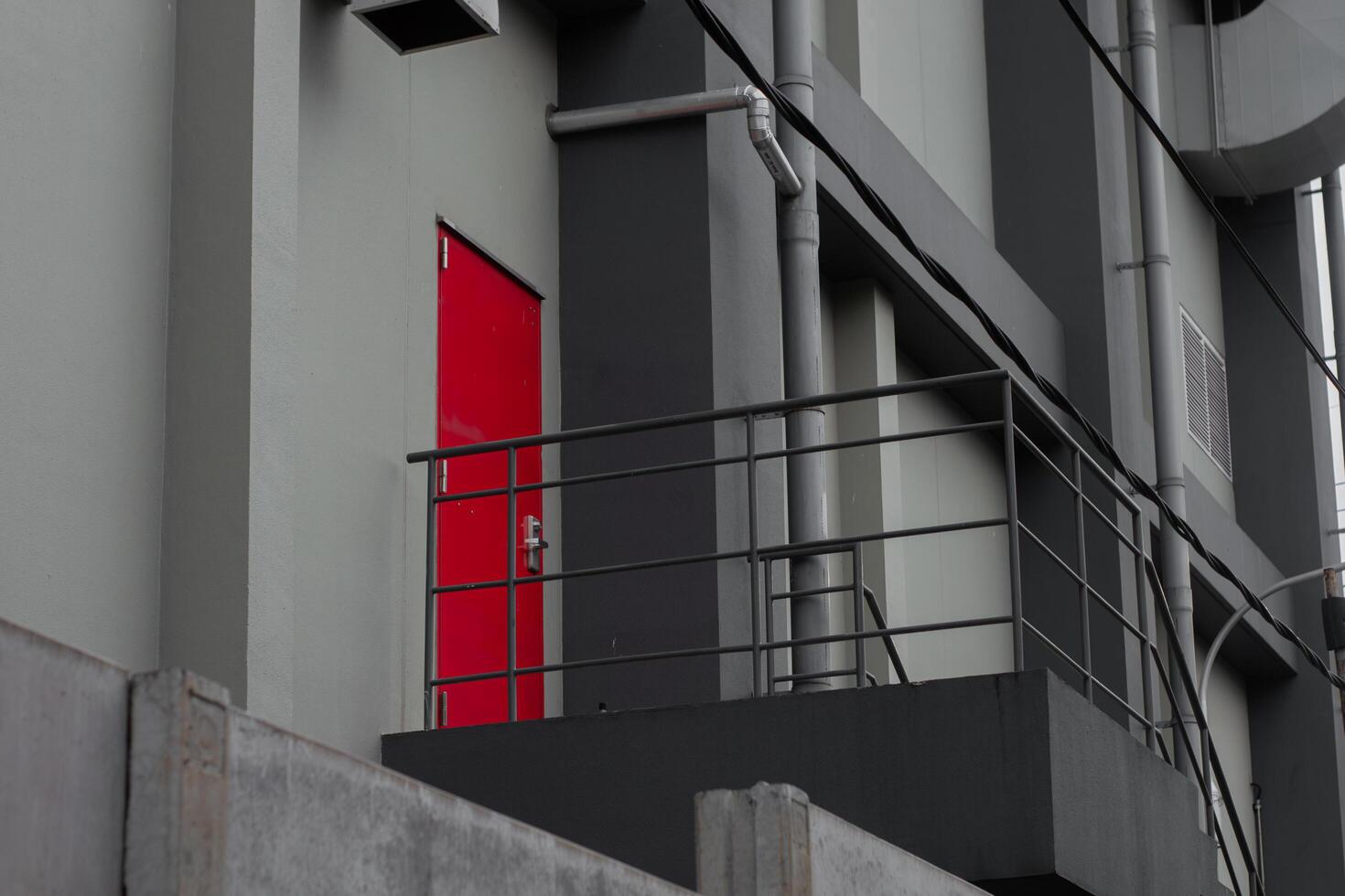 Red emergency door behind factory building with black iron stairs, gray walls and pipes. Fire exit doors. This place is an important part of work safety, evacuation access and industrial safety. photo
