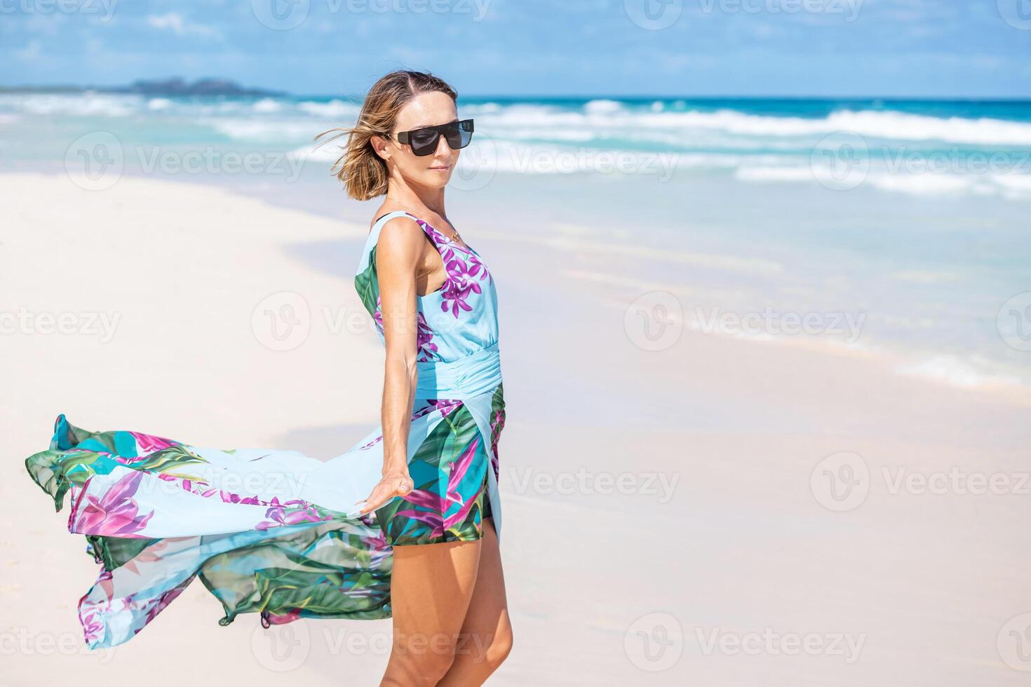 A woman in a floral dress and sunglasses on the beach photo