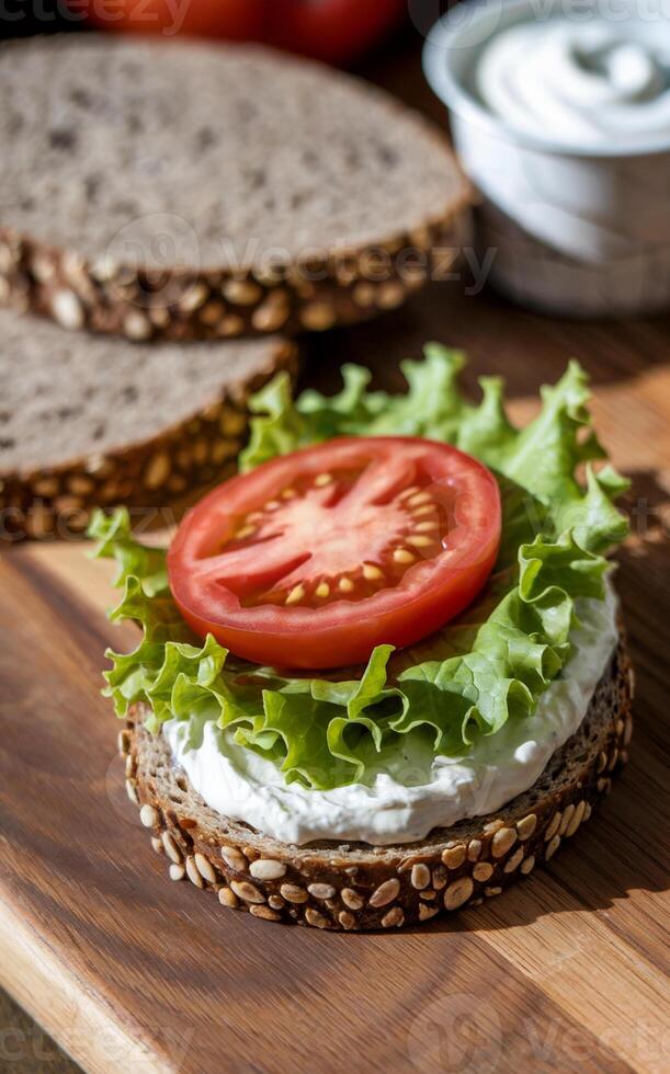 A fresh open-faced sandwich lies on a wooden board, featuring a slice of whole-grain bread topped with creamy spread, crisp lettuce, and a juicy tomato slice. photo