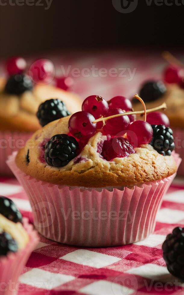A delightful muffin topped with fresh red currants and blackberries sits on a red and white checkered tablecloth. photo