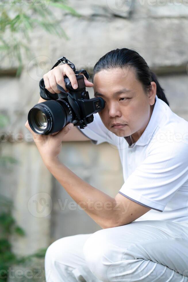 Professional Asian Chinese - Thai Camera man posture11 and focus in viewfinder and LED screen on mirrorless camera medium format in construction concrete area. photo