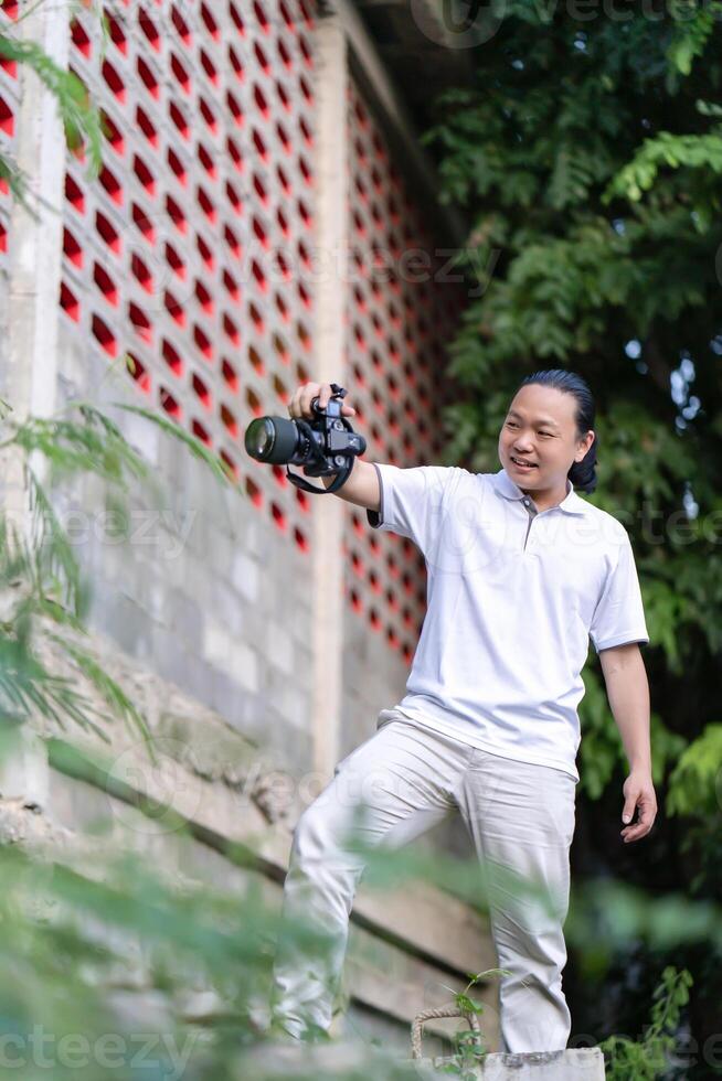 Professional Asian Chinese - Thai Camera man posture 10and focus in viewfinder and LED screen on mirrorless camera medium format in construction concrete area. photo