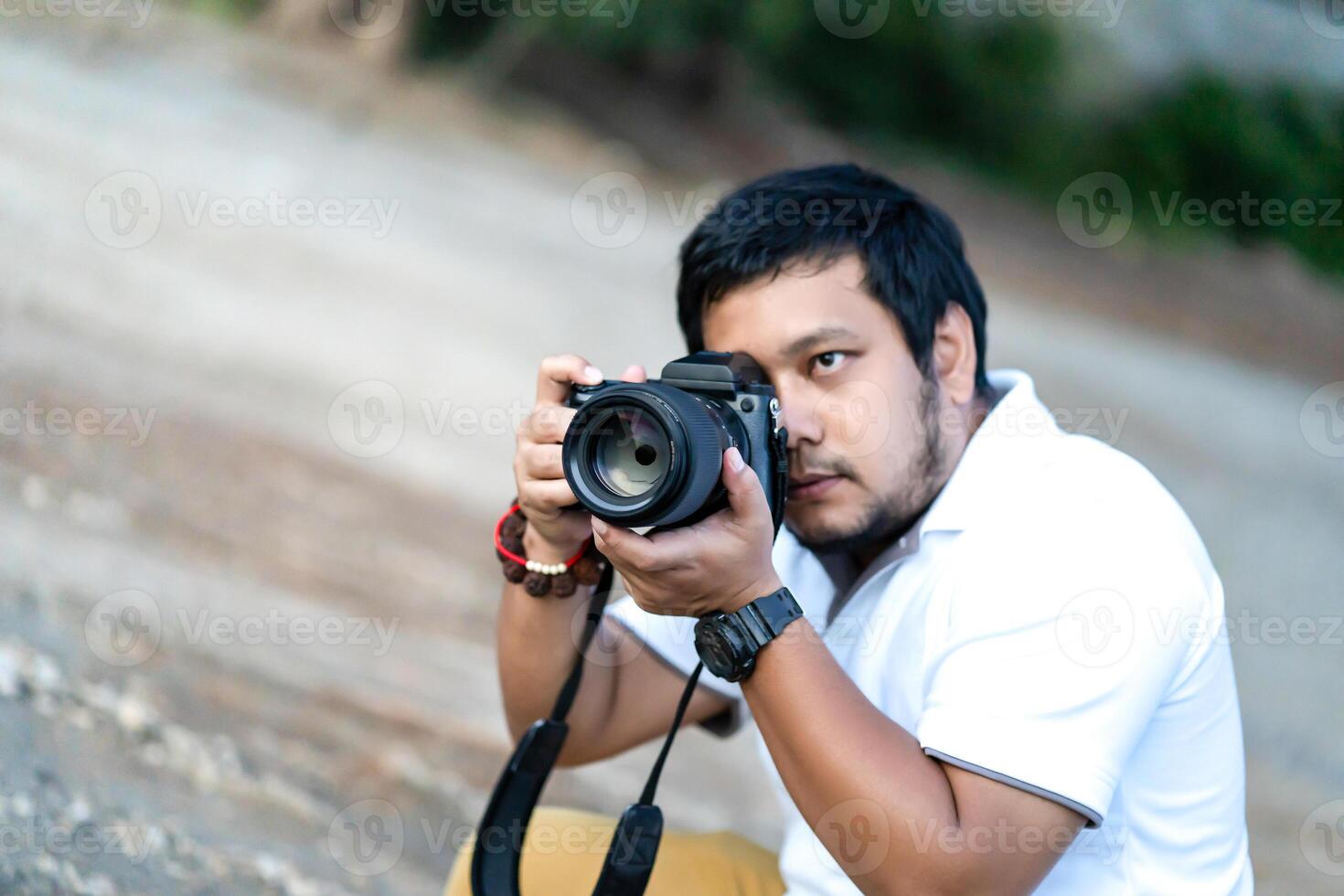 Professional Asian beard - mustache Camera man 2posture and focus in viewfinder and LED screen on mirrorless camera medium format in construction concrete area. photo