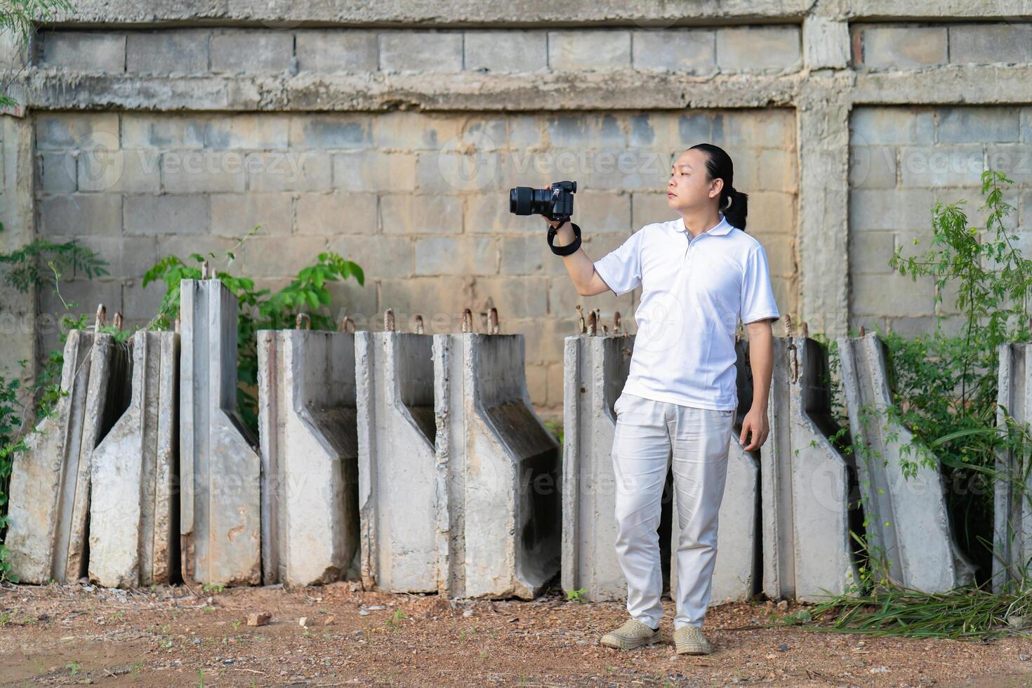 Professional Asian Chinese - Thai Camera man posture 12and focus in viewfinder and LED screen on mirrorless camera medium format in construction concrete area. photo