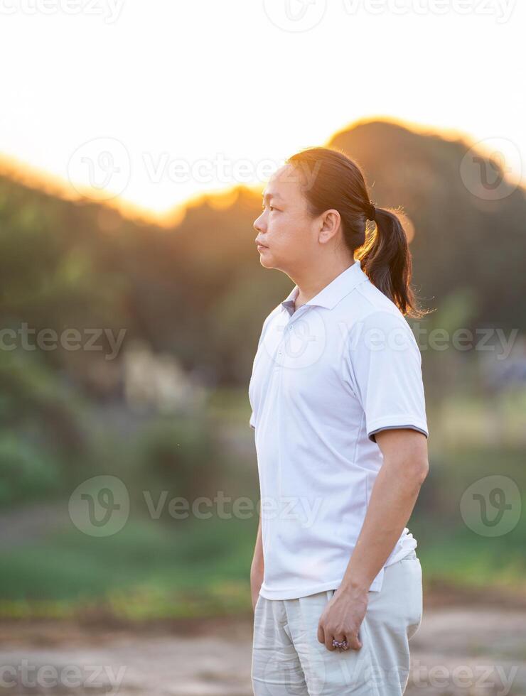 Asian Man long hair stands and relax on the dry field in golden twilight time.3 photo