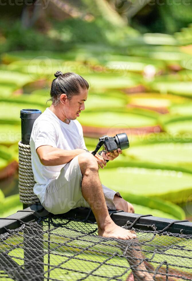 Asian Man is holding a camera and taking a photo at outdoor field with the Lily Lotus Leaf pond background.111