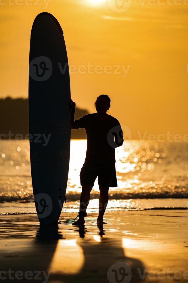 Silhouette Smart Asian Man long hair touches and poses with Standed Surfboard on the beach in Twilight time9 photo