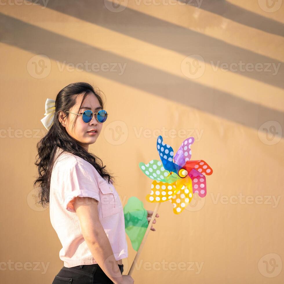 Asian woman posts and play Windmill Toy colourful rainbow colour on the building rooftop in sunset time.5 photo