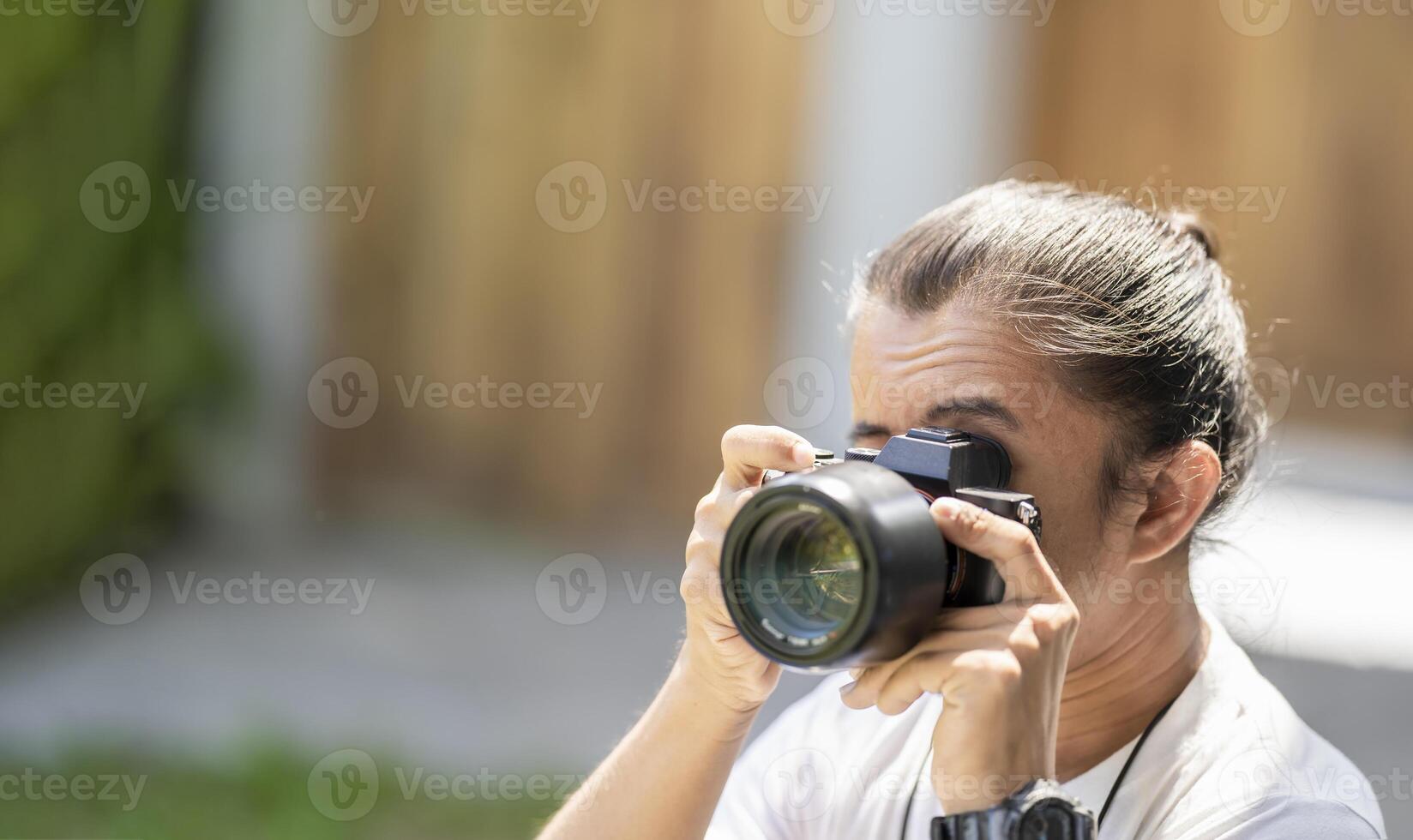 Professional Asian Camera man focus on the image with his mirrorless camera beside the street outdoor field.1 photo
