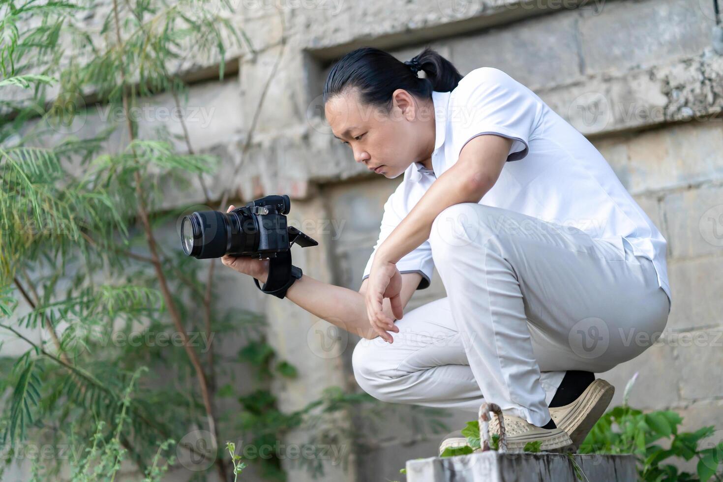 Professional Asian Chinese - Thai Camera man posture 2and focus in viewfinder and LED screen on mirrorless camera medium format in construction concrete area. photo