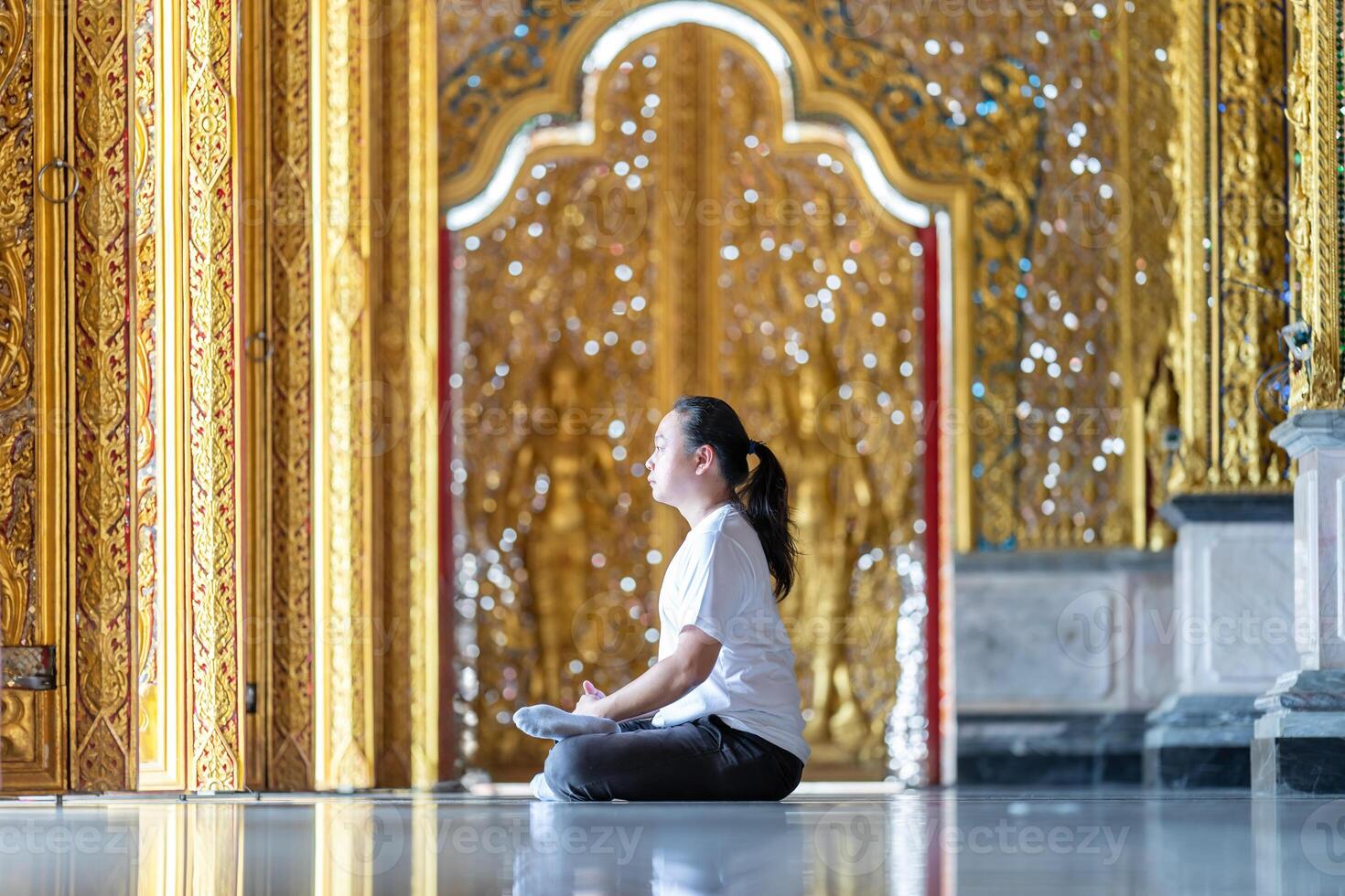 Asian Man meditates on the ground with reflection in2 the sunlight pouring into the temple church with gold gold Thai pattern blur background. photo