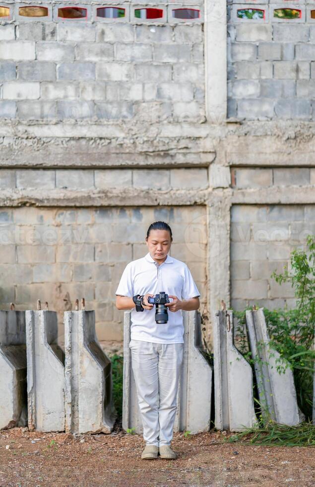 Asian Thai - Chinese professional camera man posts 4and check image shot via liveview behind Medium format Mirrorless camera with construction background. photo