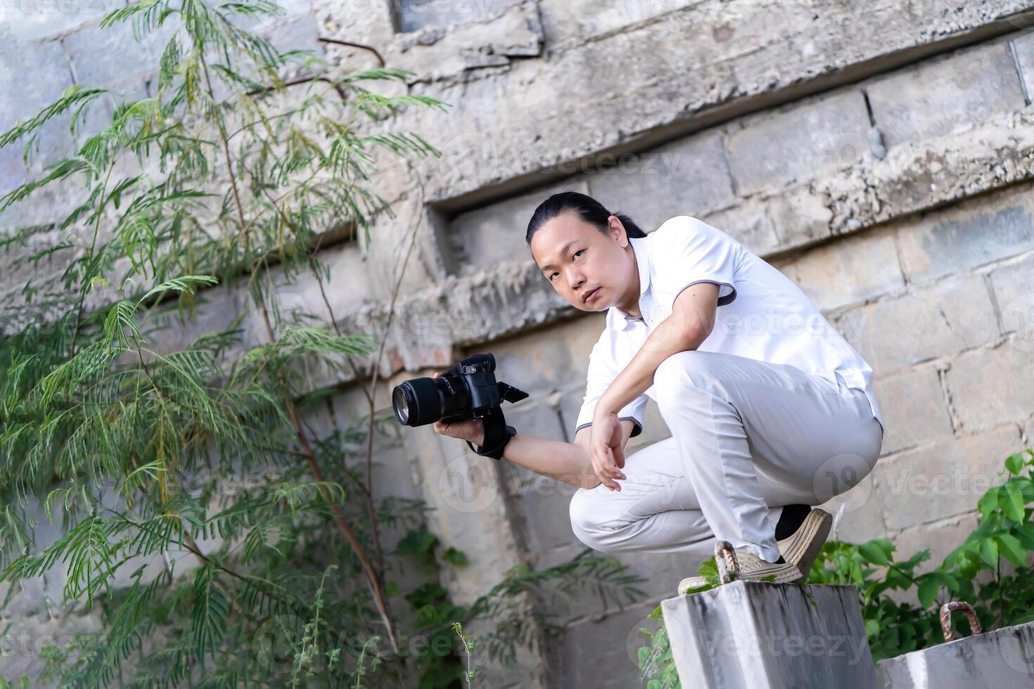Asian Professional cameraman sits and thinks about 1how to create a creativity photo in the construction area background and environment.