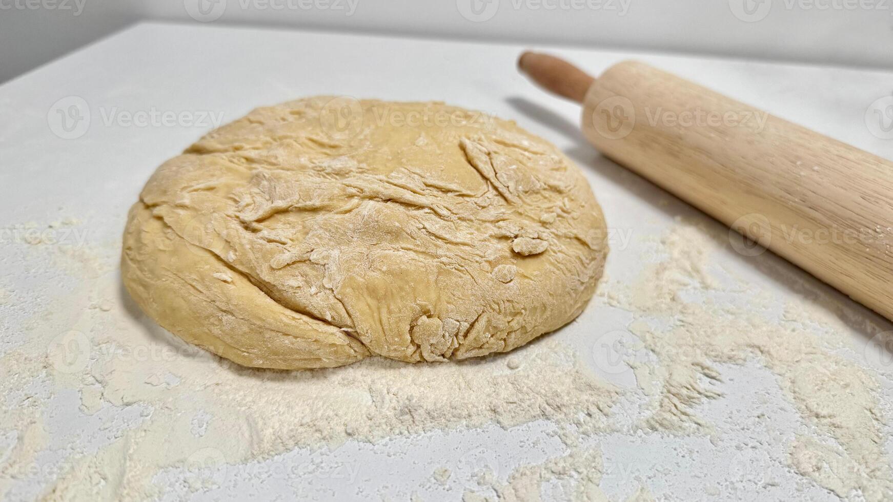 Fresh Dough Ready for Baking with a Rolling Pin and Flour Dusting. Raw dough ball on a floured surface, accompanied by a wooden rolling pin, set for baking preparations. Captures the essence of baking creativity and culinary inspiration. photo