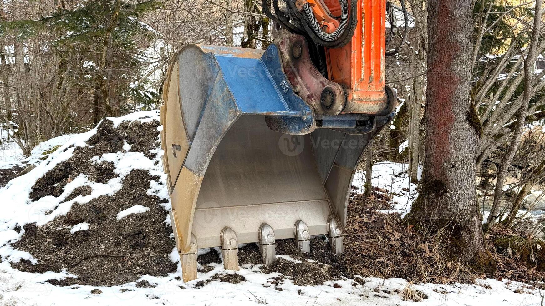 Construction Excavator Bucket by Forested Snow Landscape photo